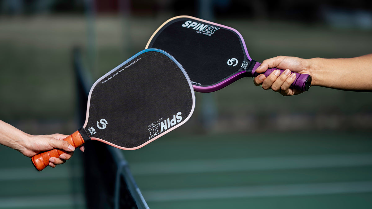 Two players holding Spinex FLEX Hybrid paddles together over the net on an outdoor court