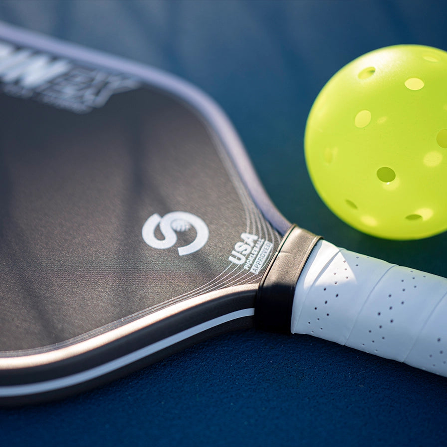 Close-up of a pickleball paddle and ball on a blue surface