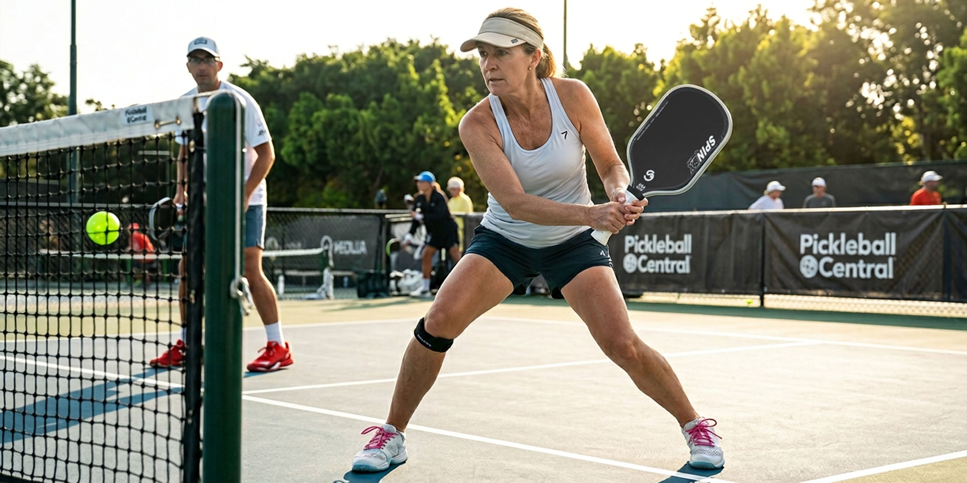 Woman playing pickleball on a court with 'Spinex Pickleball' branding.