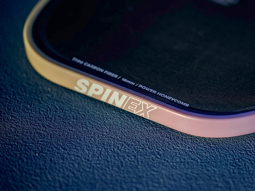 Close-up of a SPINEX pickleball paddle on a dark textured surface